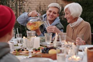 Young woman pouring a drink for an older woman. They are sitting together at a table.